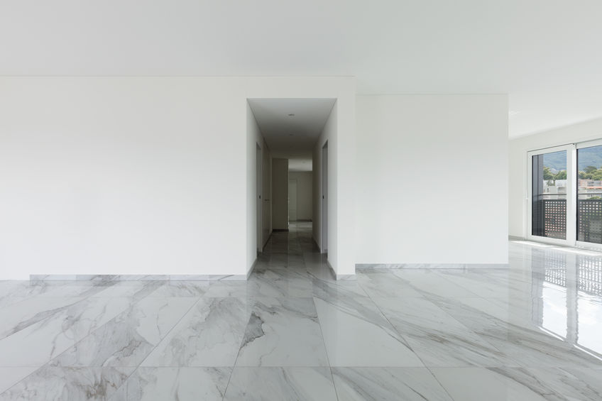 Bright, empty room with white walls and large, polished marble tile floor. Hallway visible in the background, door to balcony on the right.